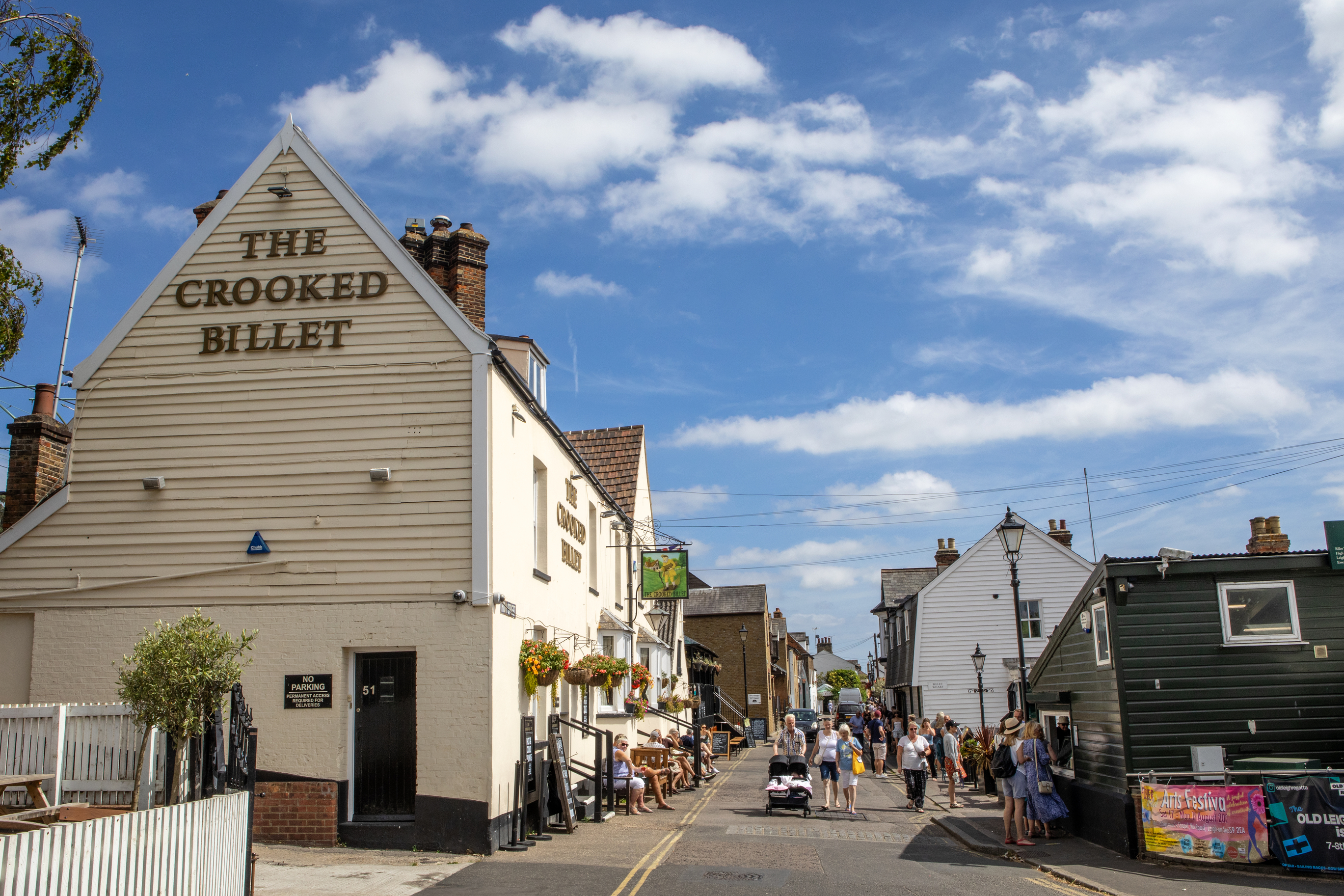 The Crooked Billet pub on Old Leigh High Street, with pedestrians and historic waterfront buildings under a blue sky.